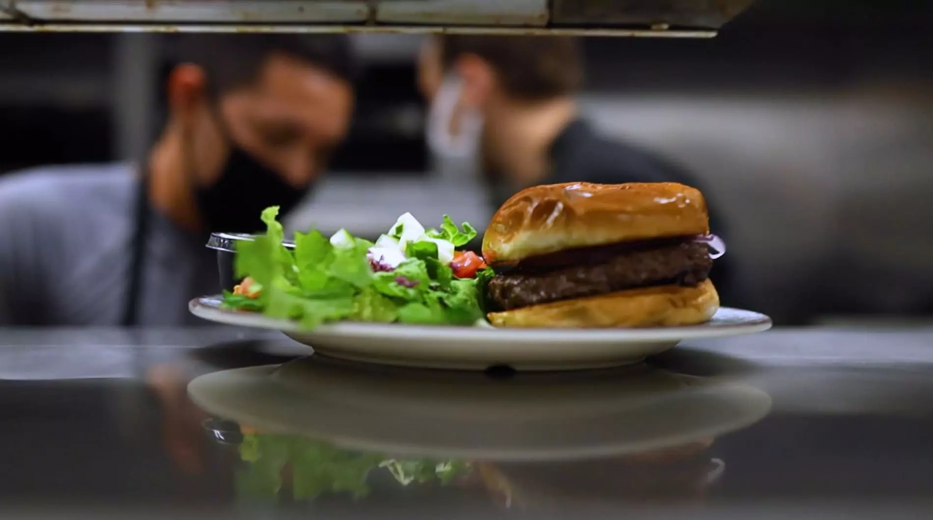 Hamburger photographed on the pass at Ivy on the Square with two chefs in the background