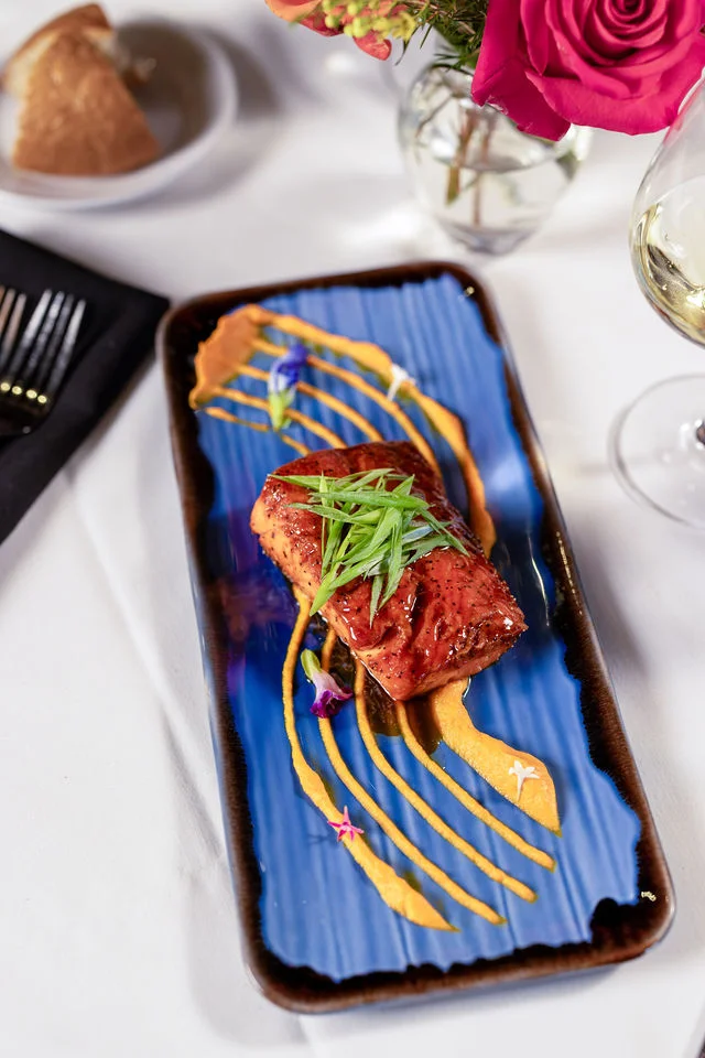 Top-down view of salmon with green garnish and golden sauce on a blue plate at Mark’s Prime
