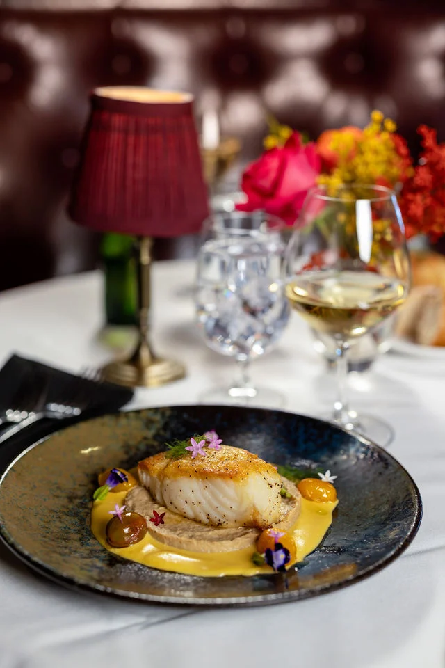 Seared fish with golden sauce and edible flowers at a white-linen table at Mark’s Prime